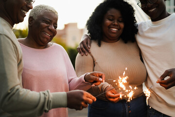 Happy african family celebrating new year's evewith sparklers outdoor at home - Focus on mother face