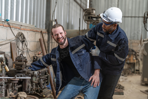 Accident in factory, male engineer feeling pain his arm got stuck in machine while working in at heavy metal industrial factory. Coworker man helping him.