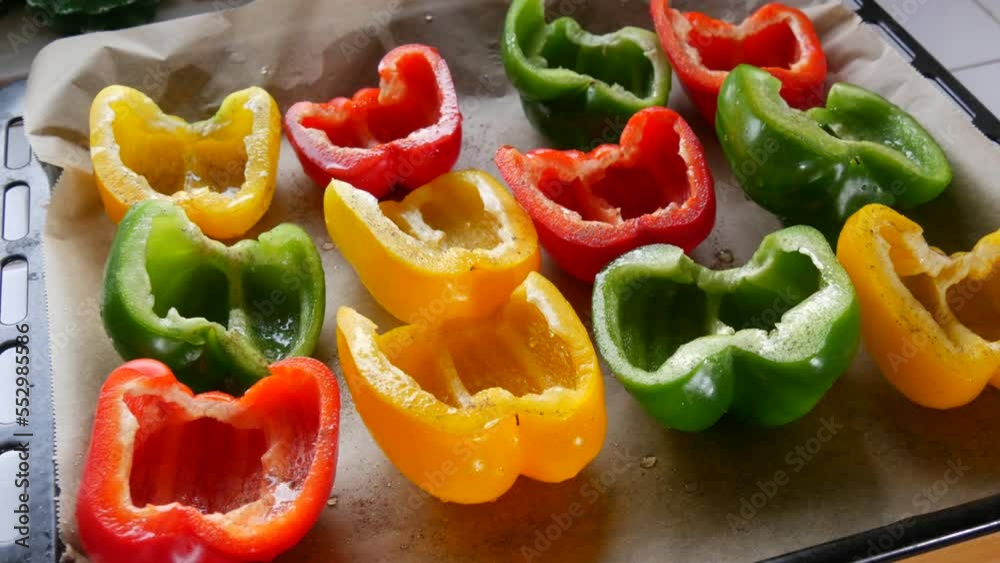 Halves of yellow, red, green paprika pepper with spices and sunflower oil lie on a baking sheet parchment before baking Halves of yellow, red, green paprika pepper with spices and sunflower oil lie on a baking sheet parchment before baking