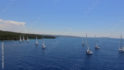 Aerial view flying over yachts competing with each other from the mediterranean sea in croatia on a bright sunny day against the backdrop of a picturesque green island. white yachts sail beautifully a photo