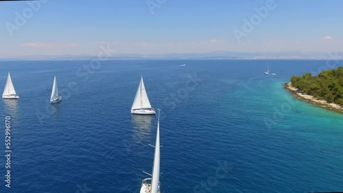 Aerial view flying over yachts competing with each other from the mediterranean sea in croatia on a bright sunny day against the backdrop of a picturesque green island. white yachts sail beautifully a photo