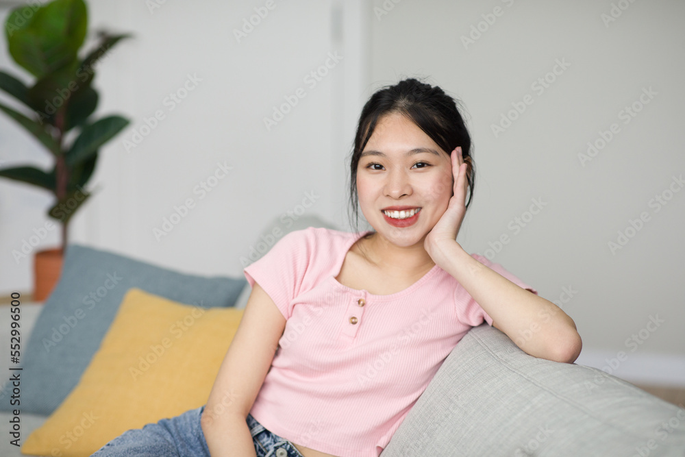 Portrait of lovely asian lady smiling and looking at camera, sitting on sofa at home, free copy space Portrait of lovely asian lady smiling and looking at camera, sitting on sofa at home, free copy space