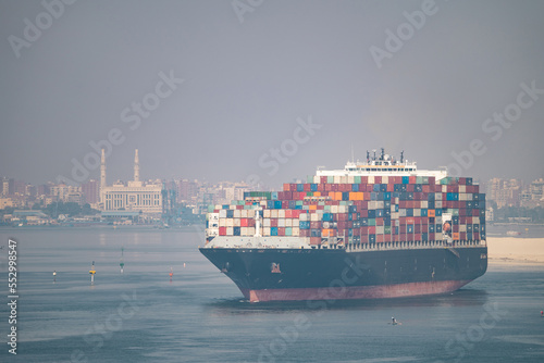 The Suez Canal is a shipping canal in Egypt. Huge Cargo ship with city on background