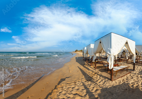 Beach tents canopies on morning paradise white sandy sea beach, Apulia, Italy.