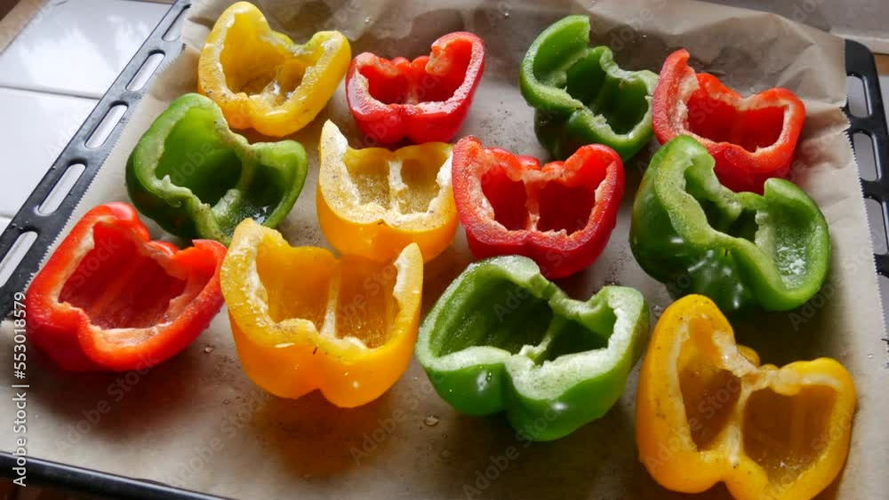 Halves of yellow, red, green paprika pepper with spices and sunflower oil lie on a baking sheet parchment before baking Halves of yellow, red, green paprika pepper with spices and sunflower oil lie on a baking sheet parchment before baking