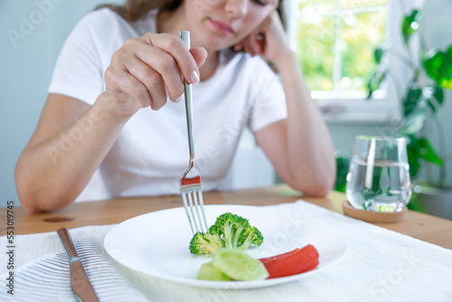 First day of diet. Unhappy young woman looking at small broccoli portion on the plate photo