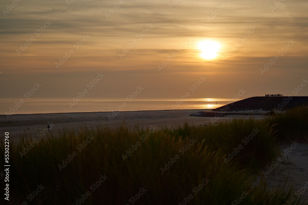 Sunset on the beach. Pastel colored sky with orange accents. Viewing platform silhouette. Grass dune in foreground. Holland, Zeeland.