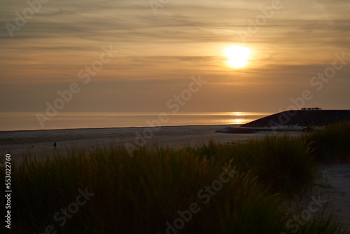 Sunset on the beach. Pastel colored sky with orange accents. Viewing platform silhouette. Grass dune in foreground. Holland  Zeeland.