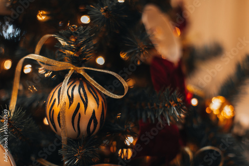 Creative Christmas ball with golden tiger pattern and ribbon hanging on the Christmas tree. Winter holiday magic season photo