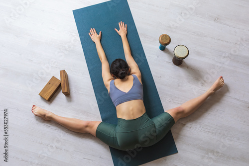 Young woman practicing yoga, performs samokanasana exercise, transverse twine with body tilt forward, lies on mat in studio, top view