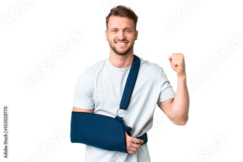 Young caucasian man with broken arm and wearing a sling over isolated chroma key background celebrating a victory