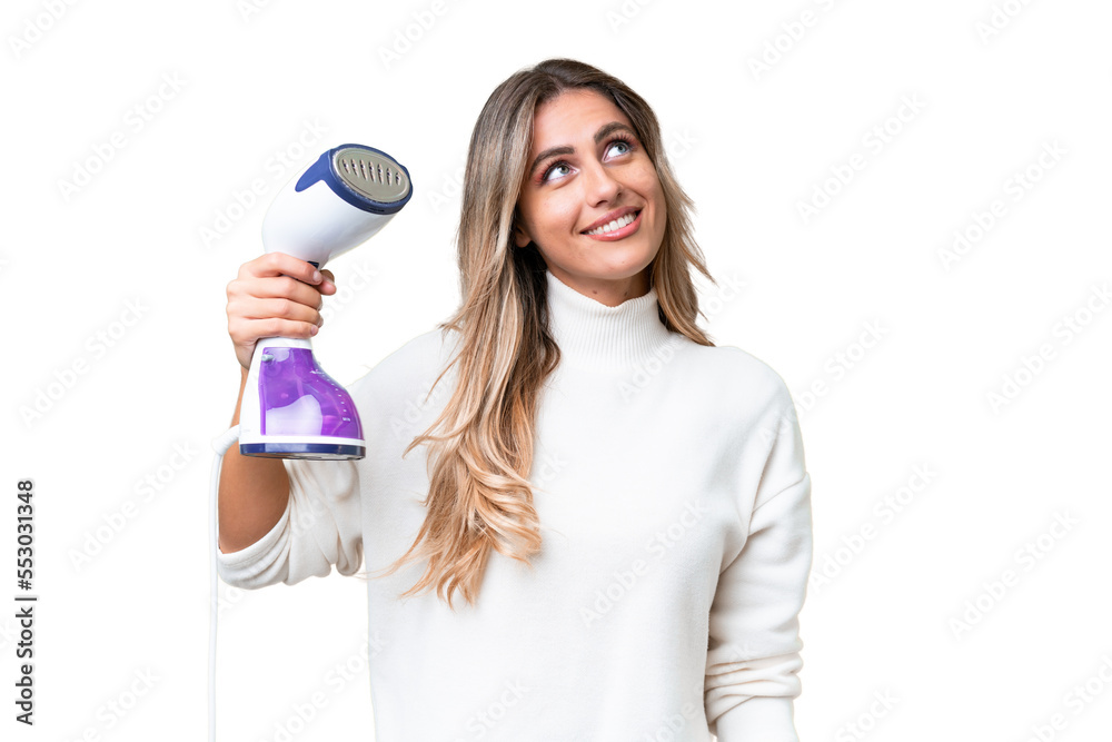 Young Uruguayan woman holding an iron over isolated background looking up while smiling Young Uruguayan woman holding an iron over isolated background looking up while smiling