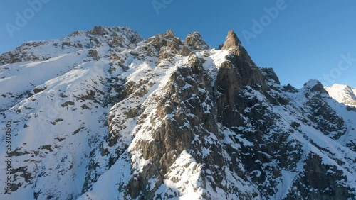 Vertiginous drone ascent of a high mountain rocky massif during a beautiful winter day