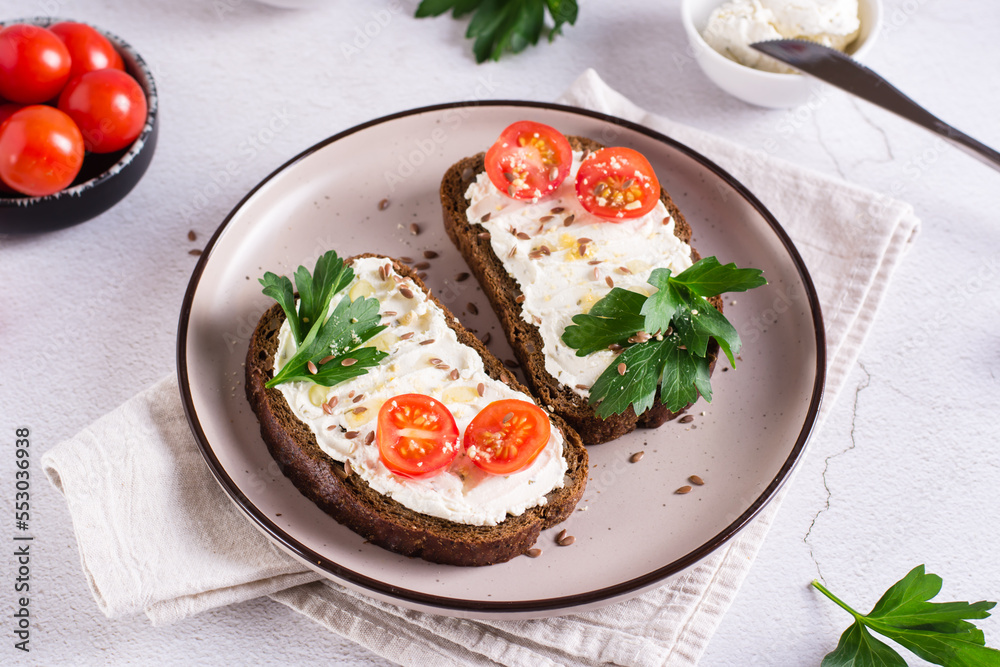 Sandwiches on rye bread with ricotta, tomatoes and parsley on a plate on the table Sandwiches on rye bread with ricotta, tomatoes and parsley on a plate on the table