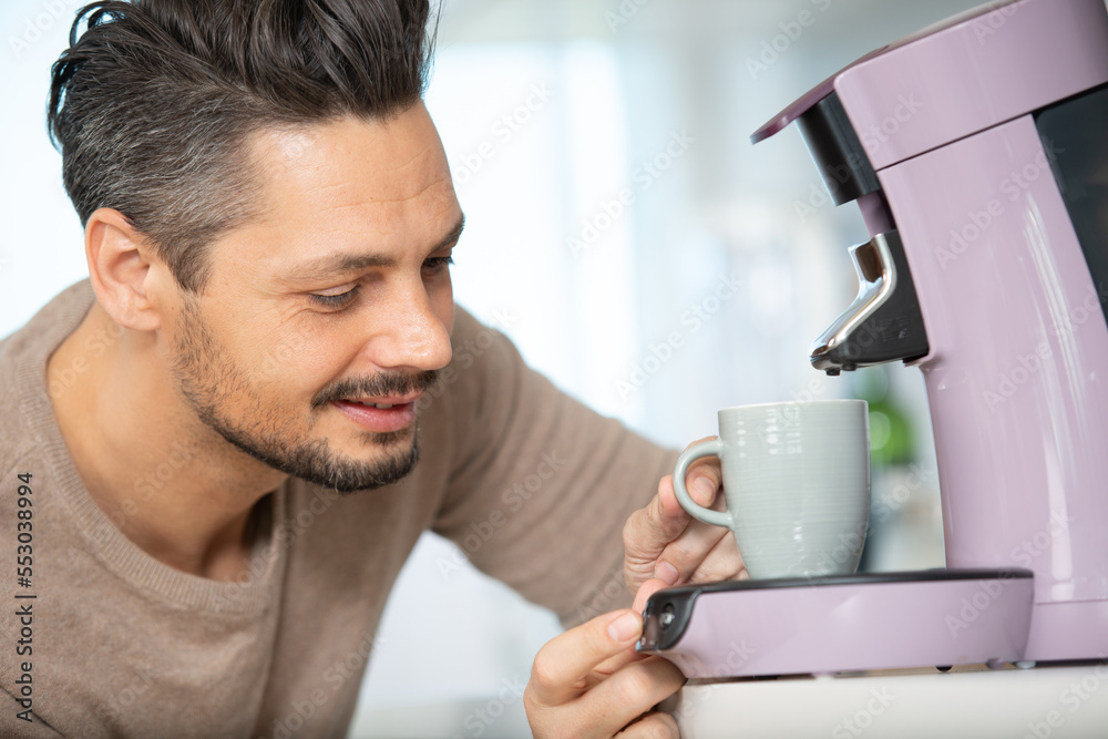 young man standing at his kitchen making coffee young man standing at his kitchen making coffee