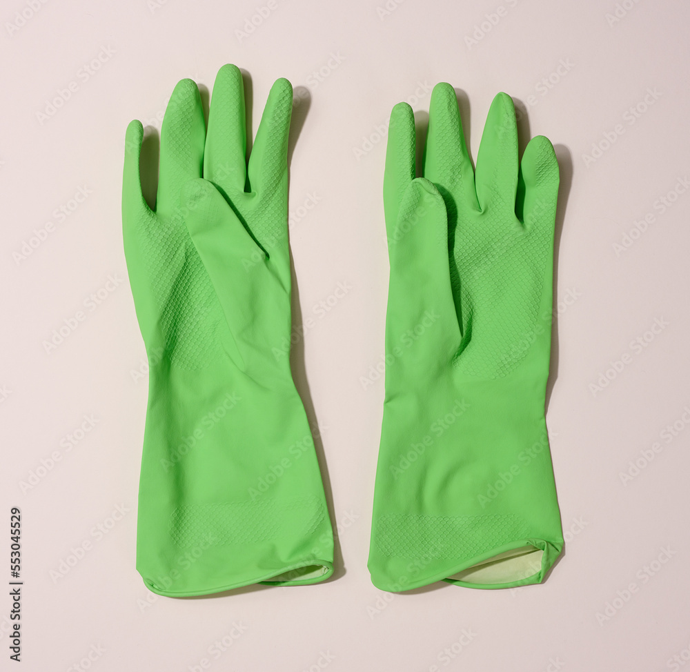 Obraz premium Pair of green protective rubber gloves for cleaning on a beige background