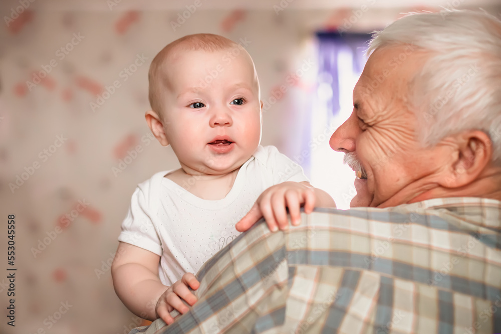 A 3-month-old baby smiles funny. Over shoulder close up of grandfather holding his baby grandson A 3-month-old baby smiles funny. Over shoulder close up of grandfather holding his baby grandson