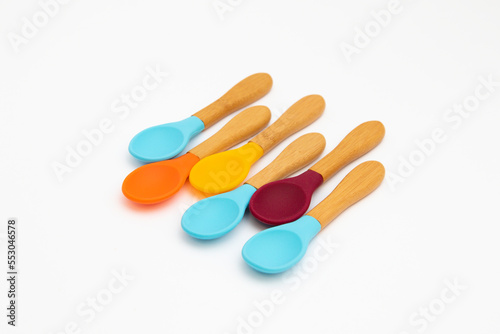 Six silicone spoons with bamboo handles of different colors on a white background. Cutlery is safe for babies