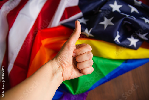 LGBT rainbow flag with american flag a person s hand makes a gesture of class and a gesture of ok. view from above. wood texture. Place for text.