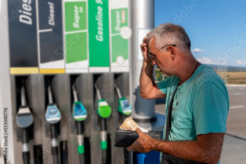 Mature man worrying and counting money, holding euro banknotes to pay high price of gasoline. Lack of money for gasoline and fuel. Expensive gasoline. Increase in gasoline prices concept. photo