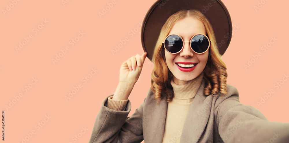 Fashionable portrait of stylish happy smiling young woman stretching hand for taking selfie with phone Fashionable portrait of stylish happy smiling young woman stretching hand for taking selfie with phone