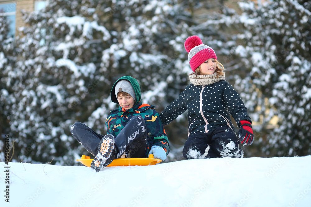 Winter portrait of children with a plastic sled sliding on a snowy slope