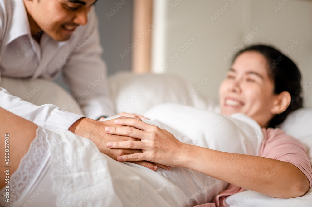 Portrait of happy pregnant wife and husband lying together on bed in bed room at home.Her husband holding wife belly.Pregnancyand motherhood  concepts.