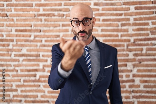 Bald man with beard wearing business clothes and glasses looking at the camera blowing a kiss with hand on air being lovely and sexy. love expression.