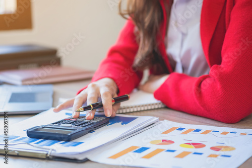 Marketing, finance, accounting, planning, a slender female accountant in a red suit using a laptop calculator and documents, charts, and graphs in company profit analysis. Business idea