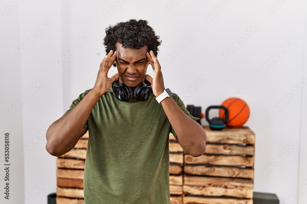 Φωτογραφία African man with curly hair wearing sportswear at the gym with hand on head for pain in head because stress