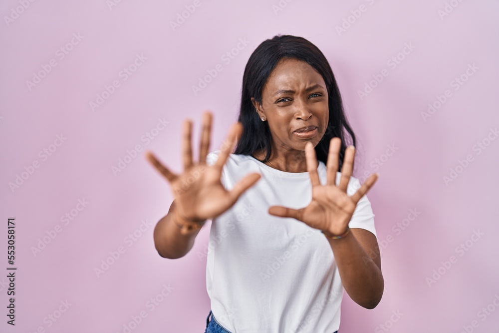 African young woman wearing casual white t shirt afraid and terrified with fear expression stop gesture with hands, shouting in shock. panic concept. African young woman wearing casual white t shirt afraid and terrified with fear expression stop gesture with hands, shouting in shock. panic concept.