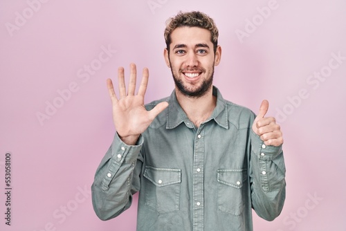 Hispanic man with beard standing over pink background showing and pointing up with fingers number six while smiling confident and happy.