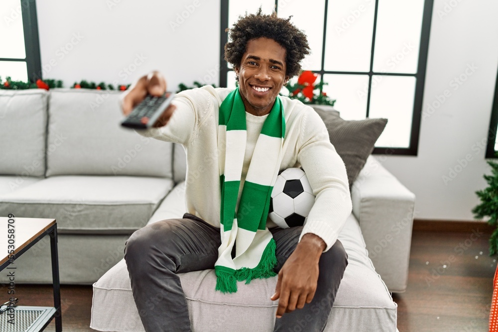 Young african american hooligan man smiling happy supporting soccer team sitting on the sofa at home. Young african american hooligan man smiling happy supporting soccer team sitting on the sofa at home.