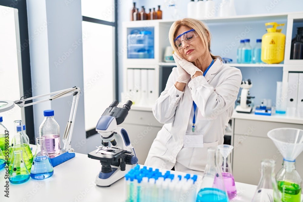 Middle age blonde woman working at scientist laboratory sleeping tired dreaming and posing with hands together while smiling with closed eyes. Middle age blonde woman working at scientist laboratory sleeping tired dreaming and posing with hands together while smiling with closed eyes.