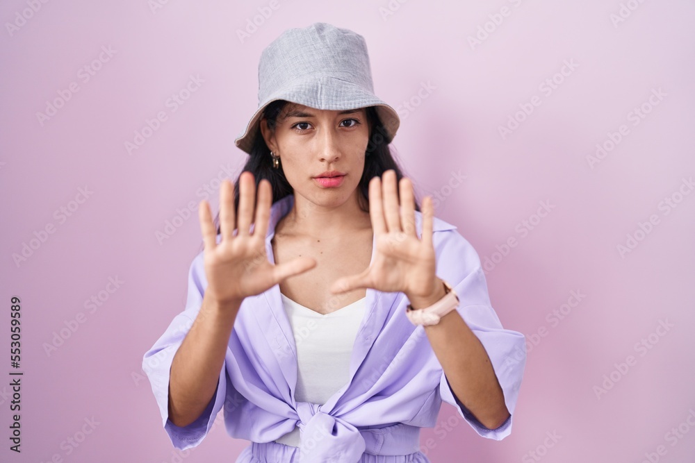 Young hispanic woman standing over pink background wearing hat moving away hands palms showing refusal and denial with afraid and disgusting expression. stop and forbidden. Young hispanic woman standing over pink background wearing hat moving away hands palms showing refusal and denial with afraid and disgusting expression. stop and forbidden.