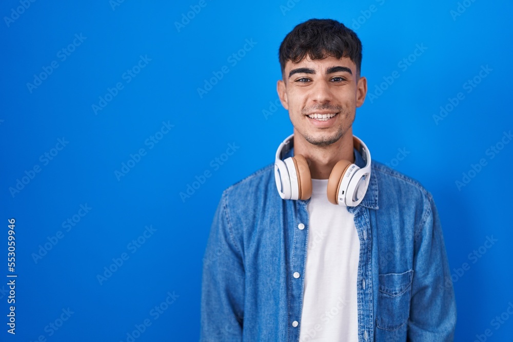 Young hispanic man standing over blue background with a happy and cool smile on face. lucky person.