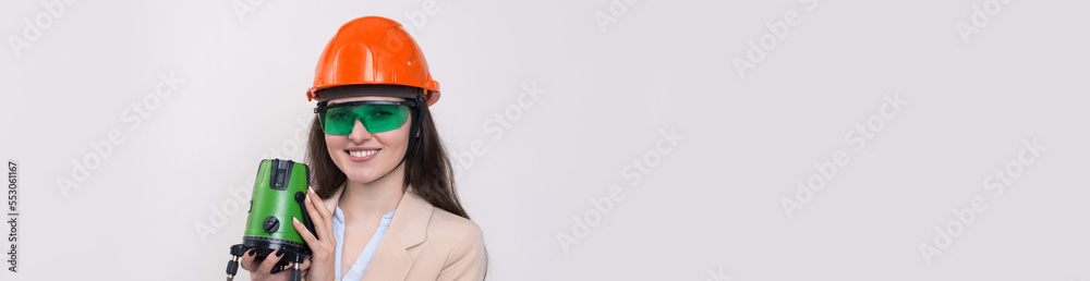 A girl in an orange helmet and a laser level in her hands on a white background. A girl in an orange helmet and a laser level in her hands on a white background.