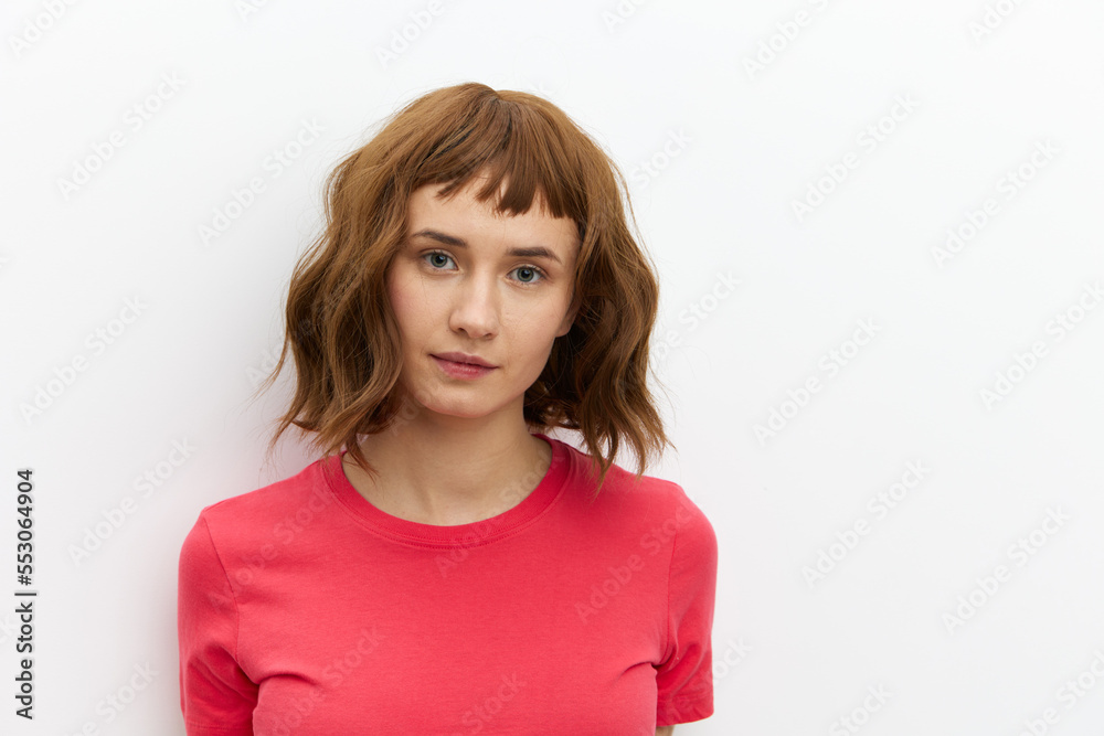 a close, horizontal portrait of a beautiful, attractive woman with short red hair standing in a red T-shirt and looking into the camera with a calm expression on her face. a close, horizontal portrait of a beautiful, attractive woman with short red hair standing in a red T-shirt and looking into the camera with a calm expression on her face.