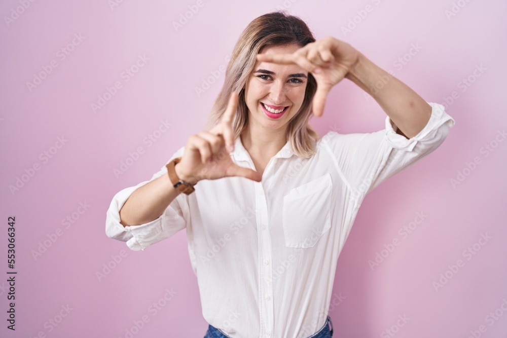 Young beautiful woman standing over pink background smiling making frame with hands and fingers with happy face. creativity and photography concept. Young beautiful woman standing over pink background smiling making frame with hands and fingers with happy face. creativity and photography concept.