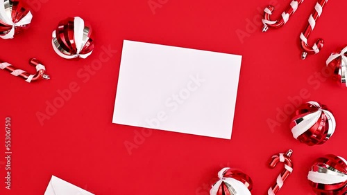 Christmas card with opening envelope with white paper on red background with ornaments. Stop motion. Flat lay