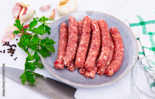 Fresh raw pork longaniza sausages ready for grilling on plate with kitchen knife, condiments and greens. Spanish cuisine