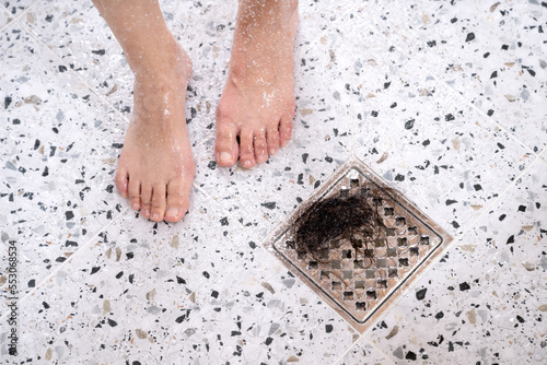 A woman suffering from alopecia is taking a shower, there is hair in the drain next to her feet photo