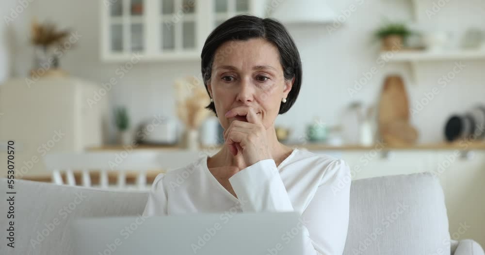 Serious middle-aged woman working on laptop at home looks at device screen thinks, search problem solutions feels undecided or hesitated, text email to client do telework remotely using internet. Tech Serious middle-aged woman working on laptop at home looks at device screen thinks, search problem solutions feels undecided or hesitated, text email to client do telework remotely using internet. Tech