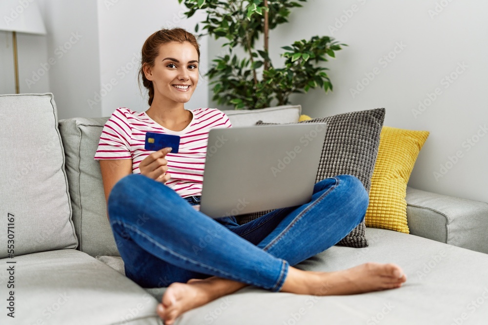Young woman using laptop and credit card sitting on sofa at home Young woman using laptop and credit card sitting on sofa at home