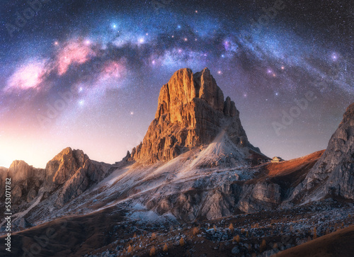 Milky Way acrh over beautifull rocks at starry night in summer in Dolomites, Italy. Landscape with purple sky with stars and bright arched milky way over high alpine rocky mountains. Space. Nature photo