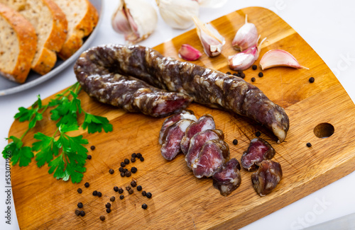 Cured pork sausage with condiments on wooden chopping board over white background. Preparing food concept.