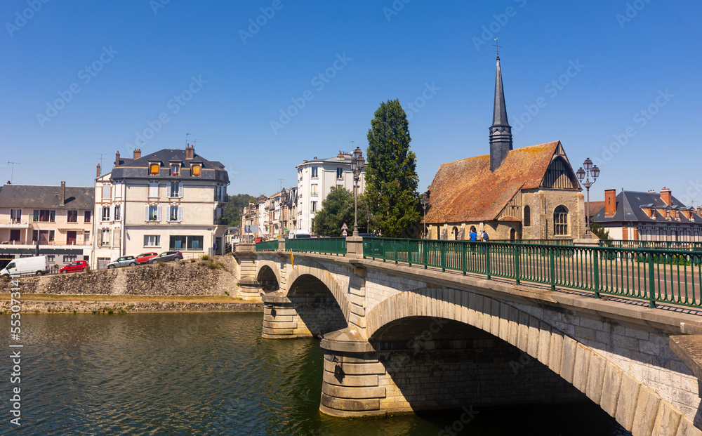 Scenic summer view of Sens townscape overlooking arched bridge across Yonne river and medieval catholic church of Saint-Maurice on embankment on sunny day, France