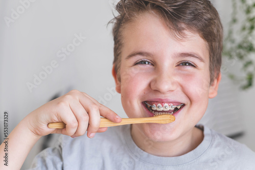 Happy boy child cleaning teeth with braces use wooden eco friendly toothbrush healthy lifestyle