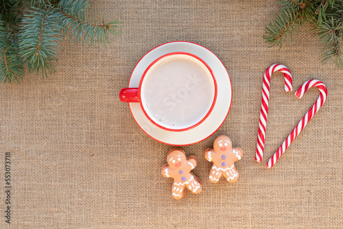 Hot winter drink - chocolate in white mug with gingerbread men and candy canes. Christmas time. Cozy home atmosphere, burlap fabric background. Holiday mood in the air