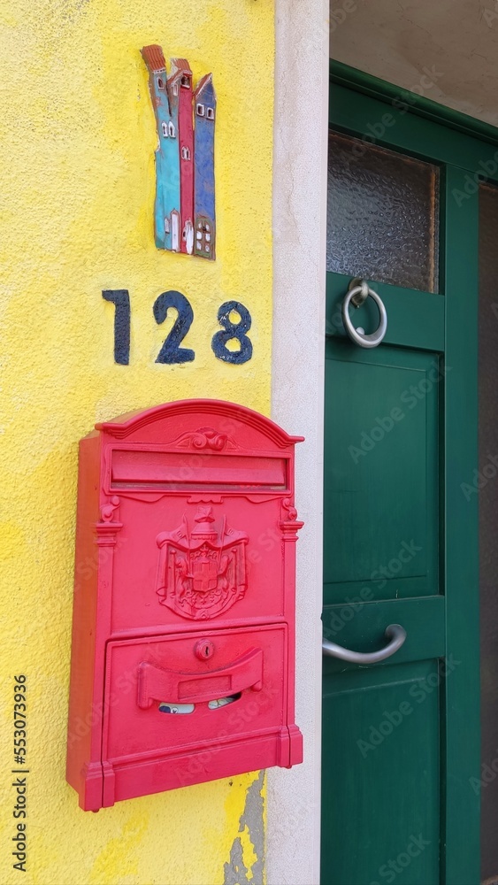 Pink mailbox on a yellow wall, next to a green door, on the island of Burano, Italy. Local flavor and traditions on the Venetian island of Burano Pink mailbox on a yellow wall, next to a green door, on the island of Burano, Italy. Local flavor and traditions on the Venetian island of Burano